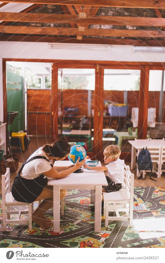 Lehrerin, die dem kleinen Jungen im Vorschulalter bei den Hausaufgaben hilft. Glück schön Ferien & Urlaub & Reisen Stuhl Tisch Kind Schule lernen Mensch Frau