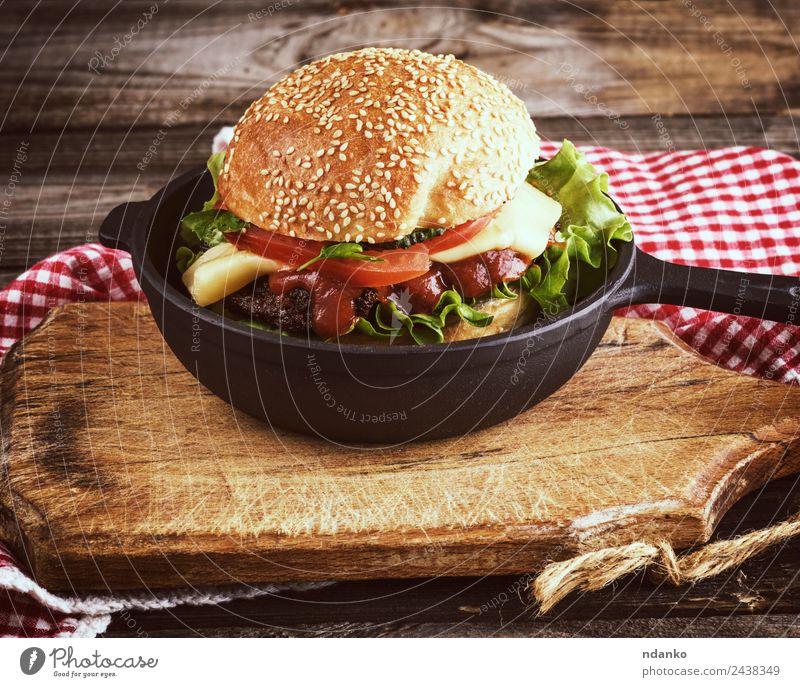 Burger mit einem Fleischklumpen Käse Gemüse Salat Salatbeilage Brot Brötchen Mittagessen Fastfood Pfanne Tisch Holz Essen frisch groß lecker grün schwarz