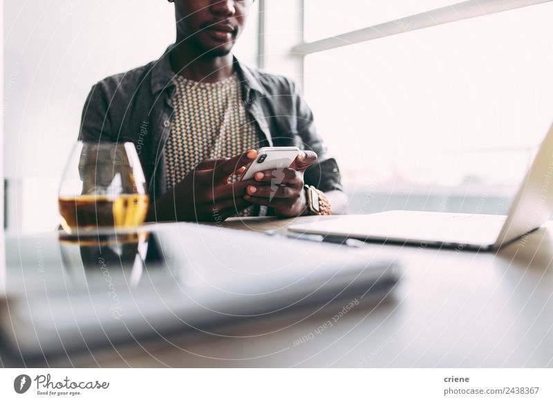 junger afrikanischer Mann, der zu Hause mit Smartphone und Laptop beschäftigt ist. trinken Design Glück Tisch Arbeit & Erwerbstätigkeit Business Telefon PDA