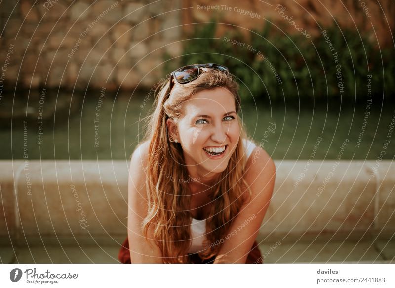 Porträt einer jungen blonden Frau, die lachend im Freien in einem Garten sitzt und in die Kamera schaut. Freude schön Gesicht Mensch Junge Frau Jugendliche