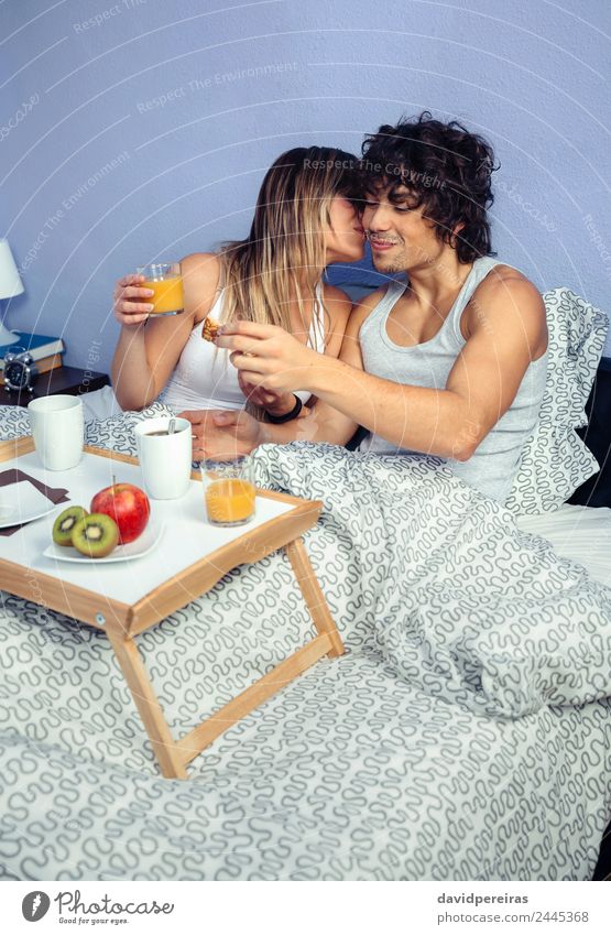 Schöne junge Frau, die sich zu einem Mann im Bett küsst. Frucht Apfel Frühstück Saft Kaffee Lifestyle Glück schön Erholung Freizeit & Hobby Schlafzimmer