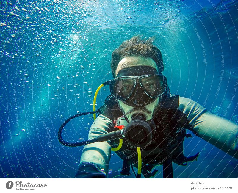 Mann mit Tauchausrüstung taucht im Meer und schaut in eine Kamera mit blauem Wasserhintergrund. Lifestyle exotisch Freude Freizeit & Hobby