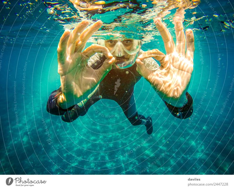 Unterwasserporträt eines Mannes, der im Meer taucht, in die Kamera schaut und mit beiden Händen das "ok"-Zeichen macht. Lifestyle Freude Freizeit & Hobby