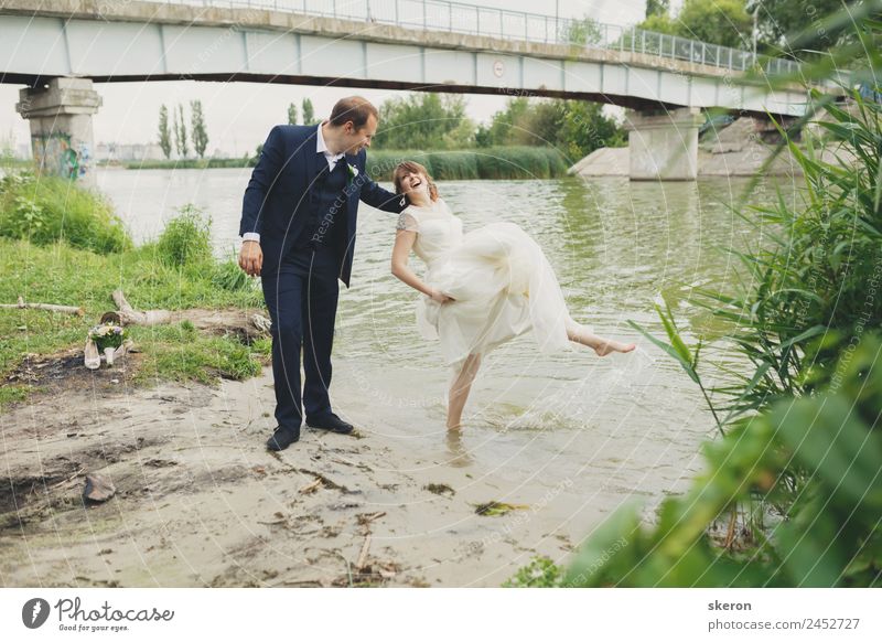 der Bräutigam hält eine lächelnde Braut, die ihre Füße in den Fluss benetzt. Lifestyle Freizeit & Hobby Sommer Wellen Valentinstag Hochzeit maskulin feminin