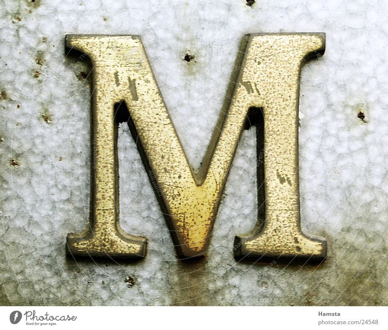 Golden M Buchstaben Serife obskur gold Metall Licht von Seite Prägung Stanzung