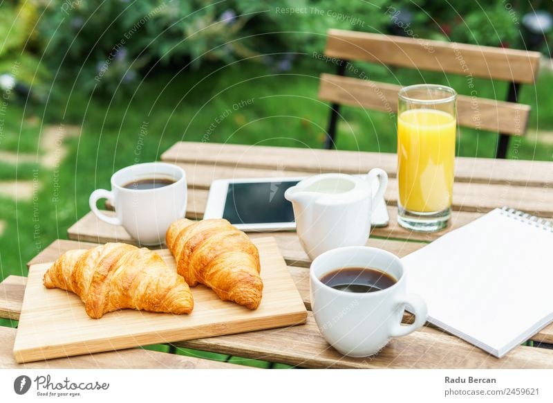 Frühstück am Morgen im Grünen Garten mit französischem Croissant, Kaffeetasse, Orangensaft, Tablette und Notizbuch auf Holztisch Tisch Hintergrundbild weiß