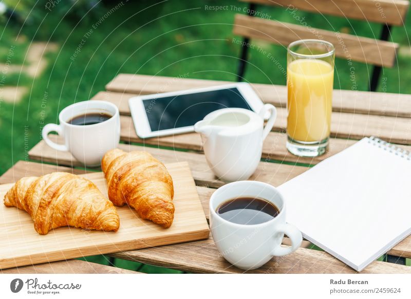 Frühstück am Morgen im Grünen Garten mit französischem Croissant, Kaffeetasse, Orangensaft, Tablette und Notizbuch auf Holztisch Tisch Hintergrundbild weiß