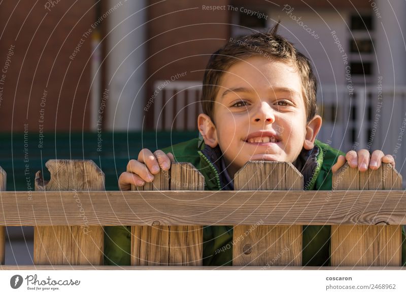 Süßer, gutaussehender Junge schaut über einen Holzzaun mit grünem Mantel. Freude Gesicht Spielen Kind Mann Erwachsene Kindheit Hand beobachten klein Neugier