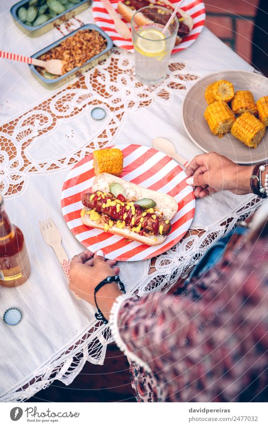 Frauenhalteplatte mit Hot Dog und Mais Wurstwaren Brot Brötchen Fastfood Limonade Alkohol Bier Teller Flasche Löffel Lifestyle Freude Glück Sommer Tisch