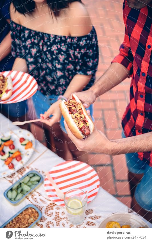 Mann hält Hot Dog im Barbecue mit Freunden. Wurstwaren Brot Brötchen Essen Fastfood Limonade Teller Lifestyle Freude Glück Sommer Tisch Frau Erwachsene