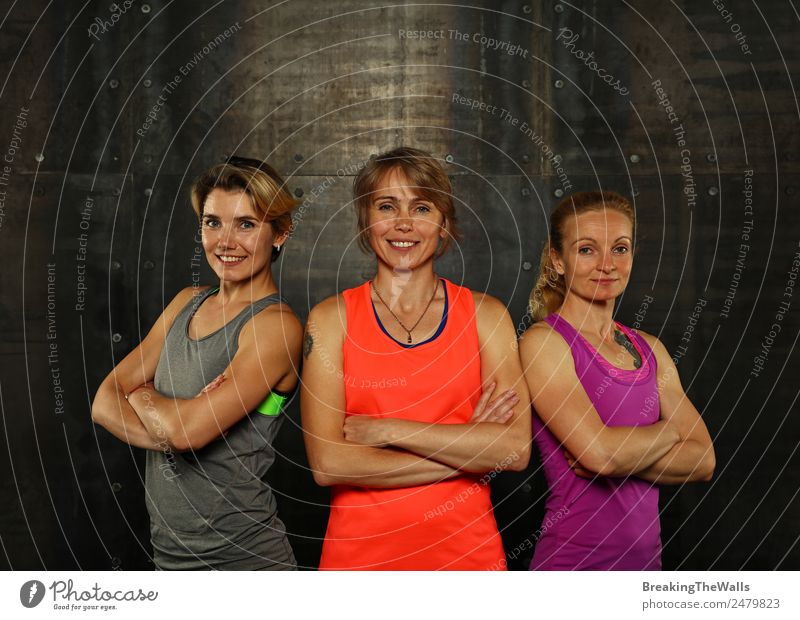Nahaufnahme von vorne Porträt von drei jungen und mittleren Alter sportliche Frauen in Sportkleidung in der Turnhalle über dunklen Hintergrund, Blick auf die Kamera