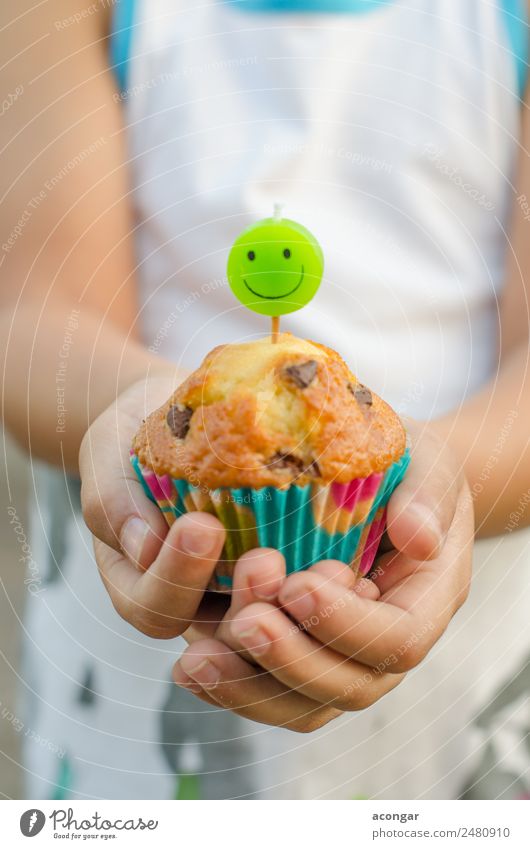 Cupcake und Kerze lächelnd in den Händen eines Kindes. Lebensmittel Dessert Glück Tisch Geburtstag Gastronomie Junge Hand 1 Mensch Papier Lächeln lecker grün