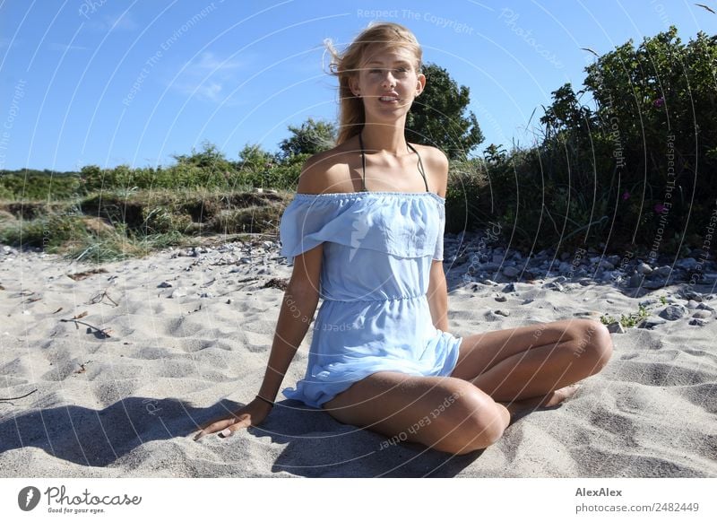 Junge Frau sitzt im Schneidersitz in einem kurzen Sommerkleid am Strand Lifestyle schön Leben Sommerurlaub Sonne Sonnenbad Jugendliche 18-30 Jahre Erwachsene