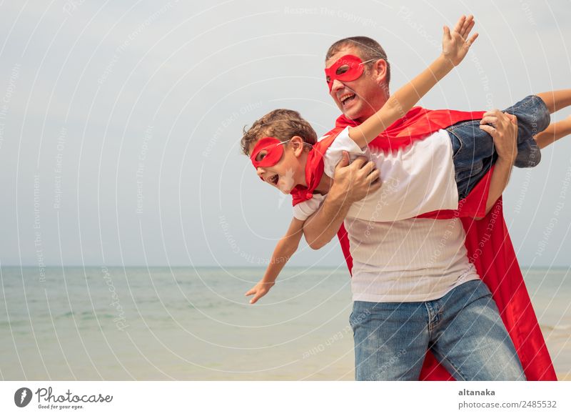 Vater und Sohn spielen tagsüber am Strand Superhelden. Die Leute haben Spaß im Freien. Konzept des Sommerurlaubs und der freundlichen Familie. Lifestyle Freude