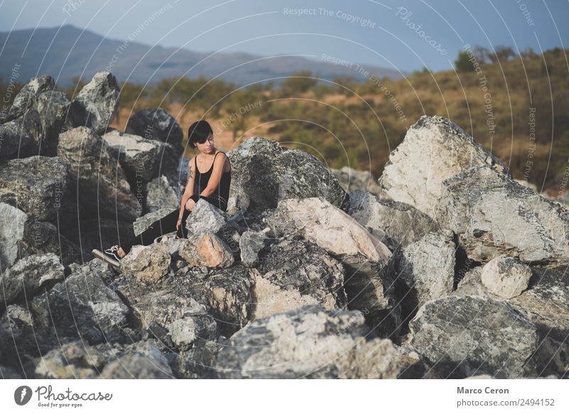 Hübsche junge Frau, die auf dem Land auf den Felsen sitzt und denkt attraktiv Hintergrund schön schwarze Kleidung brünett Fotokamera Kaukasier Landschaft Tag