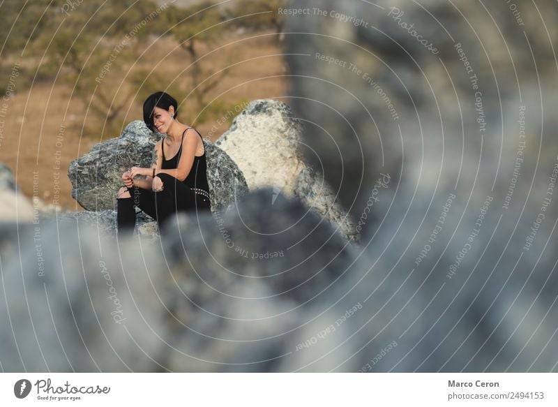 Hübsche junge Frau lächelt und sitzt glücklich auf den Felsen in der freien Natur attraktiv Hintergrund schön schwarze Kleidung brünett Fotokamera Kaukasier