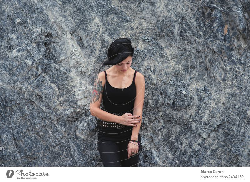 schönes brünettes, kurzhaariges Mädchen, das sich draußen an eine graue Felswand lehnt und schwarze Kleidung trägt attraktiv Hintergrund Schwarzes Haar Atmung