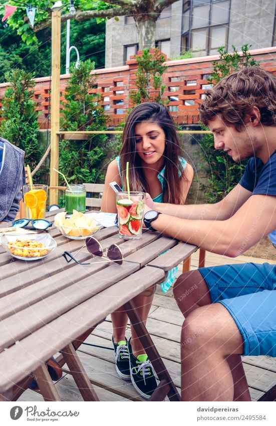 Junges glückliches Paar, das im Sommer im Freien ein Smartphone sucht. Gemüse Frucht Getränk Lifestyle Freude Glück Freizeit & Hobby Garten Tisch Telefon PDA