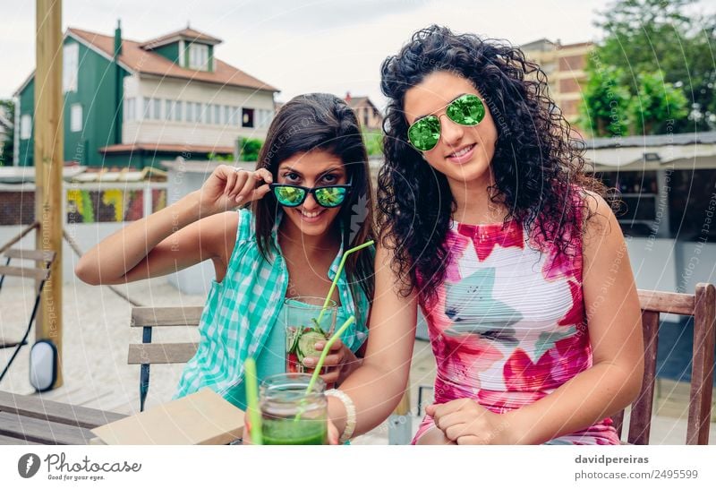 Zwei Frauen mit Sonnenbrille und Getränken, die auf die Kamera schauen. Gemüse Frucht Saft Lifestyle Freude Glück Freizeit & Hobby Sommer Mensch Erwachsene