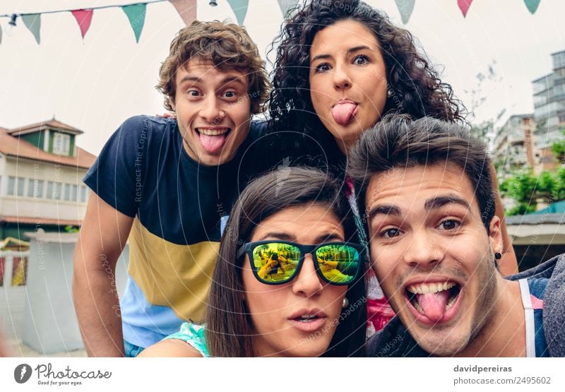 Nahaufnahme von jungen glücklichen Menschen, die in die Kamera schauen und ihre Zungen herausstrecken - Spaß auf einer Sommerparty im Freien Lifestyle Freude