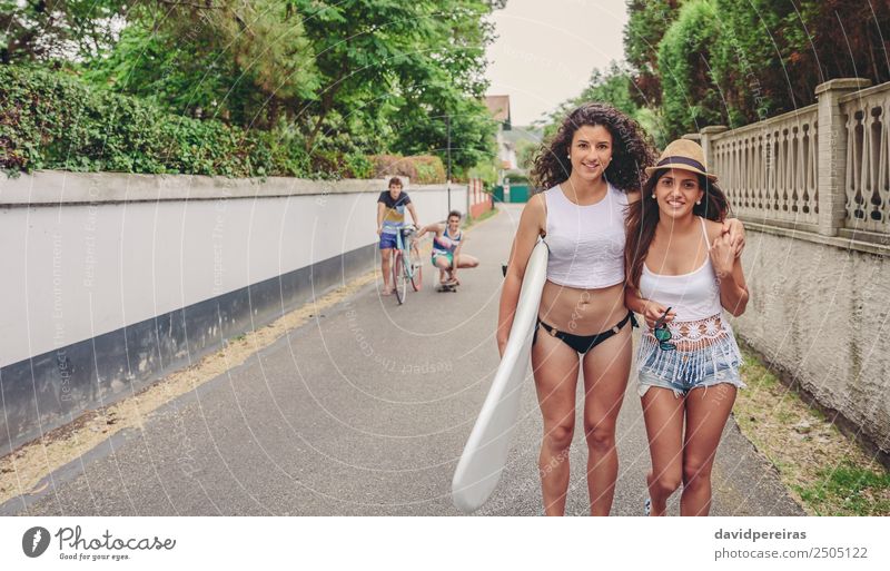 Zwei Frauen halten das Surfbrett und schauen auf die Kamera. Lifestyle Freude Glück Freizeit & Hobby Sommer Sport Erwachsene Mann Freundschaft Jugendliche