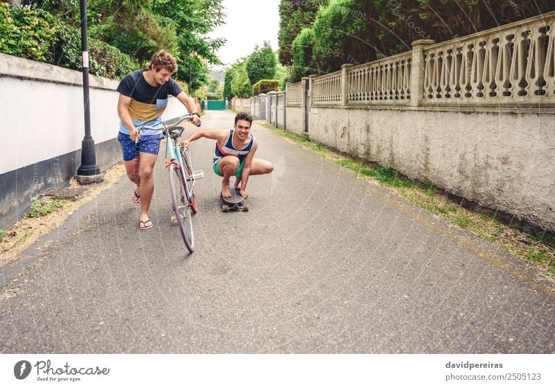 Zwei Männer, die Spaß am Fahren mit Fahrrad und Skateboard haben. Lifestyle Freude Glück Erholung Freizeit & Hobby Ferien & Urlaub & Reisen Sommer Sport Mann