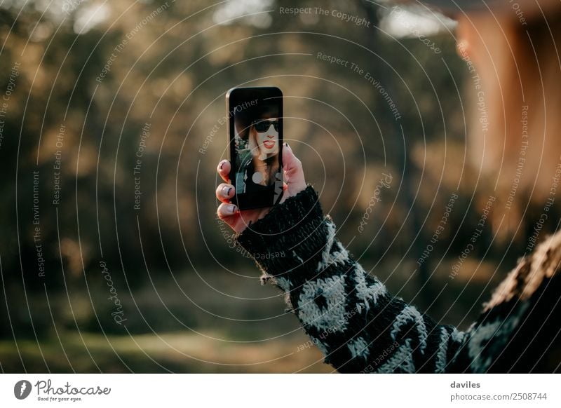 Frau, die ein Mobiltelefon in der Hand hält, um ein Selfie-Foto im Freien zu machen. Sie erscheint auf dem Bildschirm des Geräts. Lifestyle elegant Stil