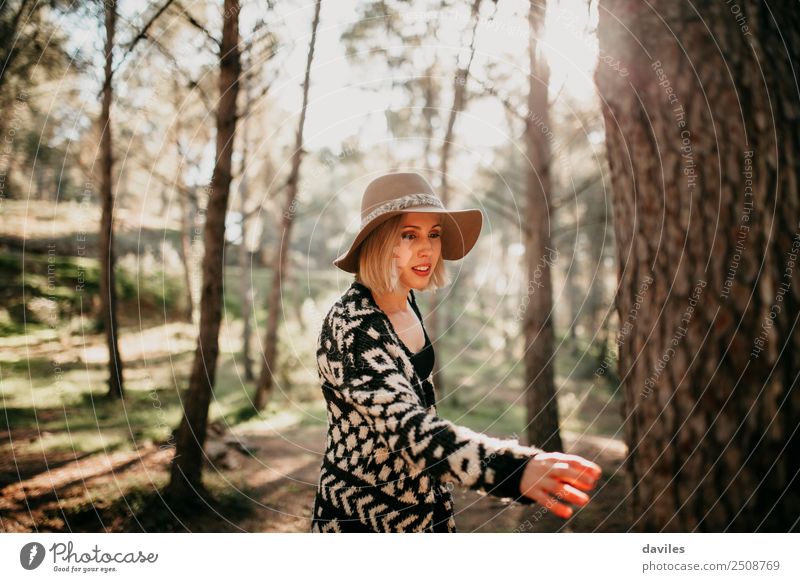 Frau, die bei Sonnenuntergang im Wald spazieren geht und mit der Hand einen Baumstamm erreicht. Lifestyle Freude Freizeit & Hobby Mensch feminin Junge Frau