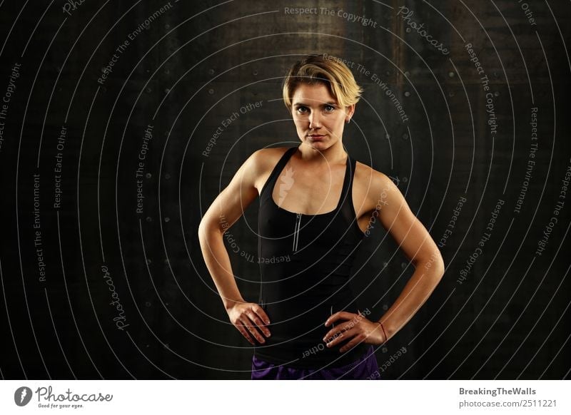 Close up vorderen Oberkörper Porträt eines jungen sportlichen Frau in Sportkleidung in der Turnhalle über dunklen Hintergrund, Blick auf die Kamera Lifestyle