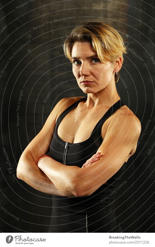 Close up vorderen Oberkörper Porträt eines jungen sportlichen Frau in Sportkleidung in der Turnhalle über dunklen Hintergrund, Blick auf die Kamera Fitness