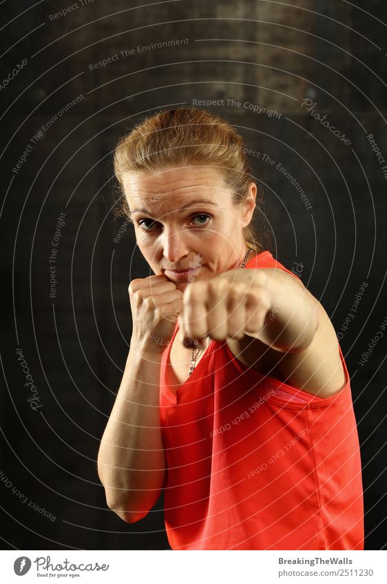 Nahaufnahme von vorne Porträt eines jungen Mitte Erwachsene sportliche Frau in Sportkleidung in der Turnhalle über dunklen Hintergrund, stehend in Boxhaltung mit Händen und Fäusten, Blick auf die Kamera