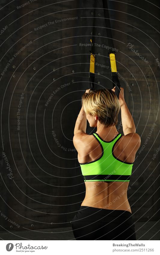 Rückansicht Porträt einer jungen sportlichen Frau beim Crossfit-Training, die mit Trx Suspension Fitness-Bänder über dunklen Hintergrund trainiert Lifestyle