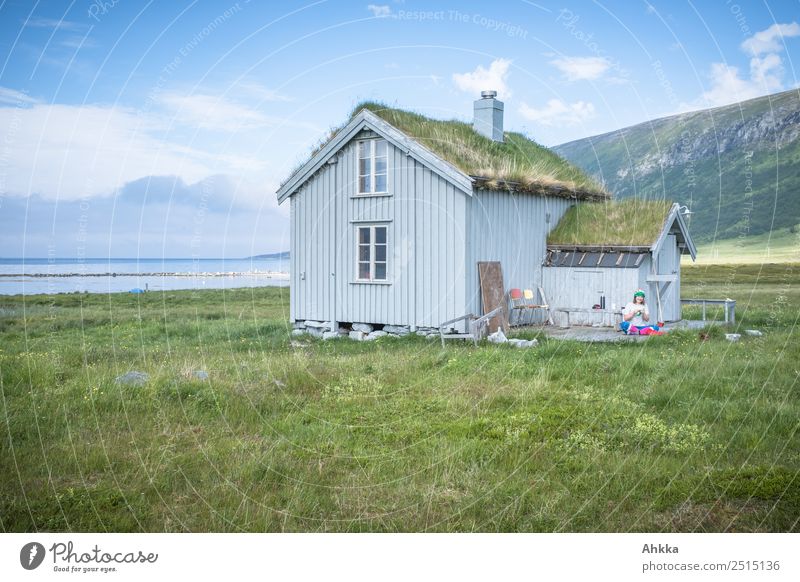 Idyllische Holzhütte am Fjord mit bewachsenem Dach bei gutem Wetter und mit junger strickender Frau in Norwegen harmonisch Wohlgefühl Zufriedenheit Erholung
