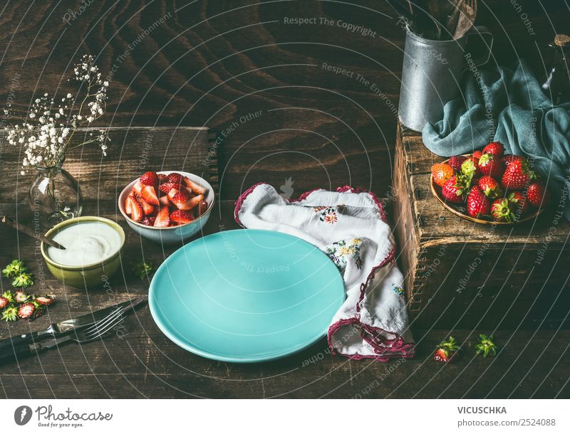 Leerer blauer Teller auf dunklem, rustikalem Holzküchentisch mit Erdbeeren und Joghurt in Schalen. Landhausstil mit Beeren im Hintergrund, Stilleben. Platz für Ihr Design, Ihre Rezepte, Ihren Text oder Ihre Produkte