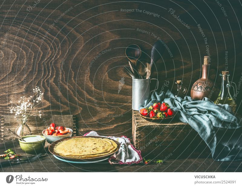 Ländliches Stilleben mit hausgemachten Crêpes auf dunklem, rustikalem Holzküchentisch mit Erdbeeren und Joghurt in Schalen . Land Stillleben selbstgemacht