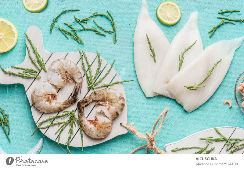 Rohe Garnelen oder Garnelen und Tintenfische auf hellblauem Hintergrund, dekoriert mit Seegras und Zitrone, Draufsicht, flach gelegt. Konzept zum Kochen von Meeresfrüchten