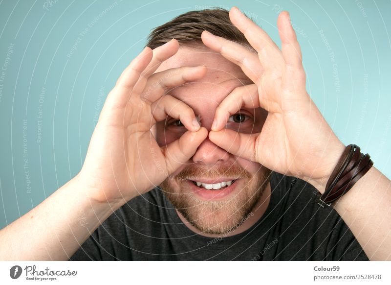 Junger Mann macht mit seinen Fingern eine Geste um seine Augen Stil Mensch maskulin Jugendliche Kopf Freundlichkeit Fröhlichkeit communication eyeglasses eyes