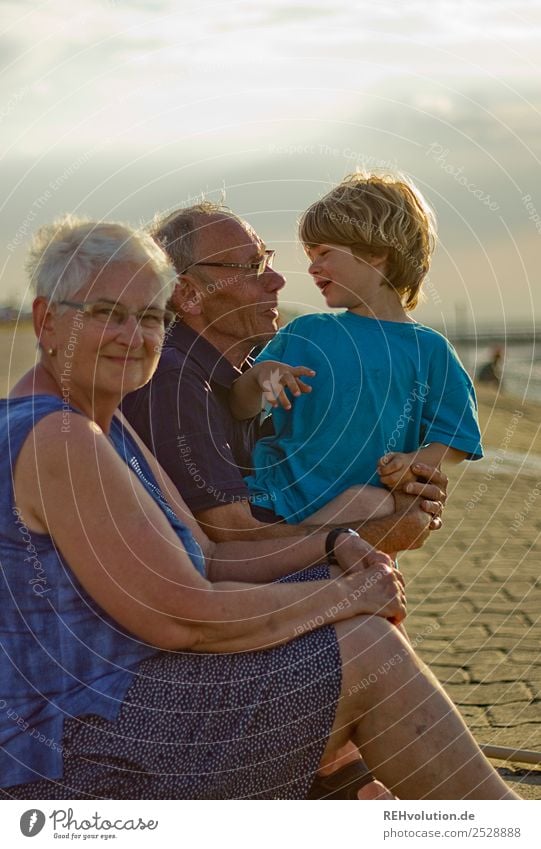 Oma und Opa mit Enkel am Strand Glück Zusammensein lachen Lächeln Sonnenlicht Sommerurlaub Großmutter Großvater Kindheit 3-8 Jahre 60 und älter