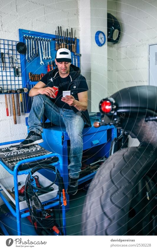 Motorradmechaniker, der sich ausruht und ein Bier trinkt. trinken Lifestyle Stil PDA Mensch Mann Erwachsene Fahrzeug sitzen authentisch retro Pause Mechaniker