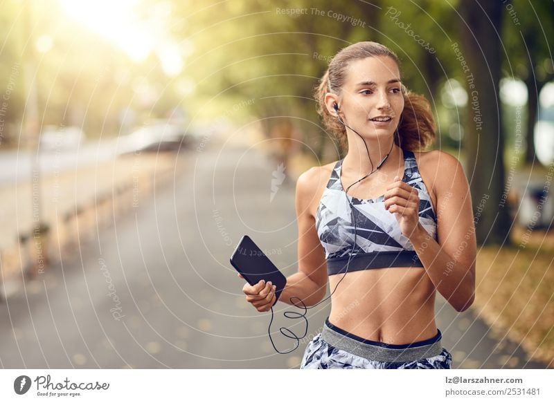 Sportliche junge Frau beim Joggen Lifestyle Sommer Musik PDA Erwachsene 1 Mensch 18-30 Jahre Jugendliche Wärme Park Straße Fitness Lächeln rennen Gesundheit