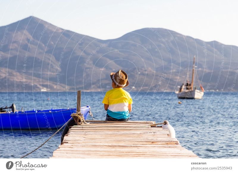 Kleiner Junge auf einem Dock, der auf dem Rücken sitzt und auf den Ozean schaut. Lifestyle Freude Glück Freizeit & Hobby Ferien & Urlaub & Reisen Sommer Strand