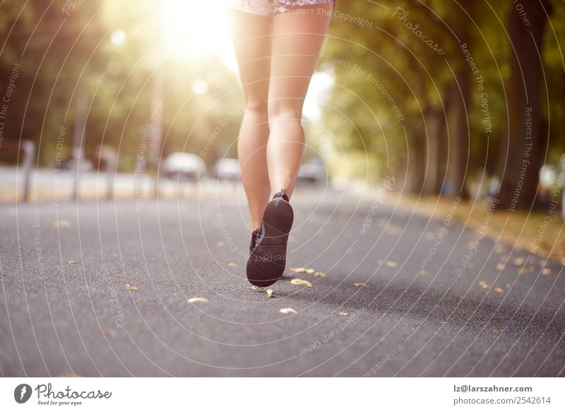 Junge Frau beim Joggen auf einer Herbststraße Lifestyle Erholung Sommer Sonne Sport Mensch Erwachsene Fuß Straße Schuhe Fitness hinten rennen Beine Winkel
