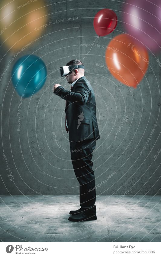 Geschäftsmann steht mit VR-Headset auf Betonboden und hält roten Ballon in der Hand vor vielen anderen bunten Luftballons Lifestyle Freude Freizeit & Hobby
