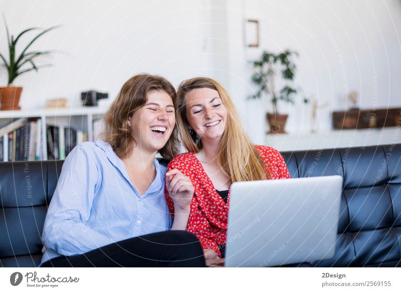 Zwei junge Frauen benutzen den Computer, während sie auf der Couch sitzen Lifestyle kaufen Glück Geld schön Leben Erholung Haus Sofa Geldinstitut Telefon PDA