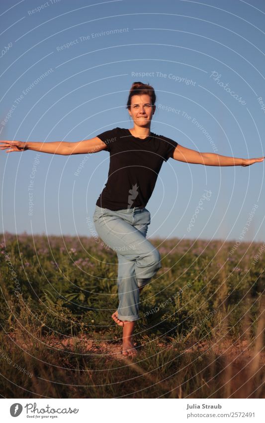 Hübsche Frau macht Yoga Übung auf einem Feld feminin Erwachsene 1 Mensch 30-45 Jahre Sonnenlicht Sommer Schönes Wetter Blume Gras Wiese T-Shirt Jeanshose