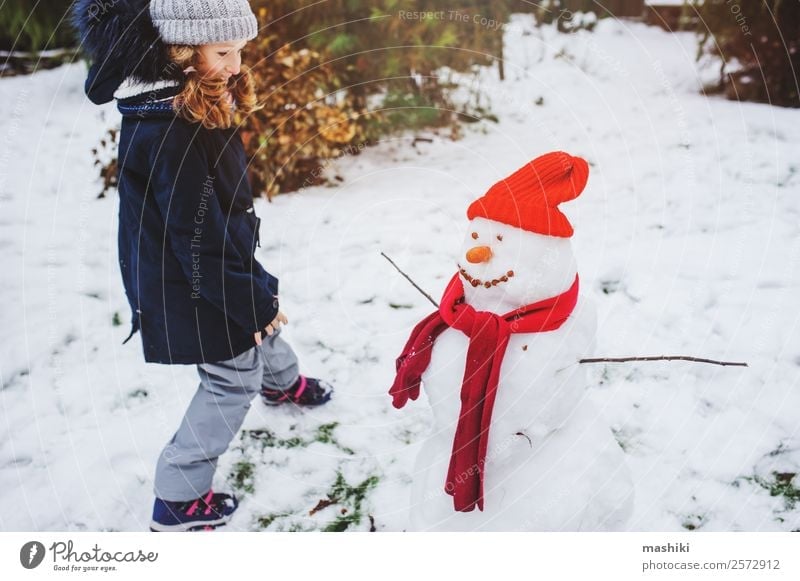 glückliches Kind Mädchen macht Schnee Mann Freude Freizeit & Hobby Spielen Ferien & Urlaub & Reisen Winter Garten Natur Wetter Park Bekleidung machen Schneemann