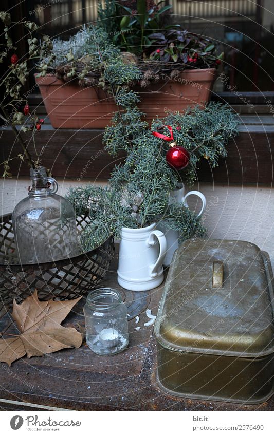 Rustikale, schöne Weihnachtsdekoration mit Zweigen und Christbaumkugel, auf altem, vintage Tisch im Winter zur Adventszeit. Gesteck zu Weihachten mit Blumentopf, Teelicht, Glasvase, Pflanzen, Hangebutte auf altem Herd, draussen im kalten, eisigenGarten.