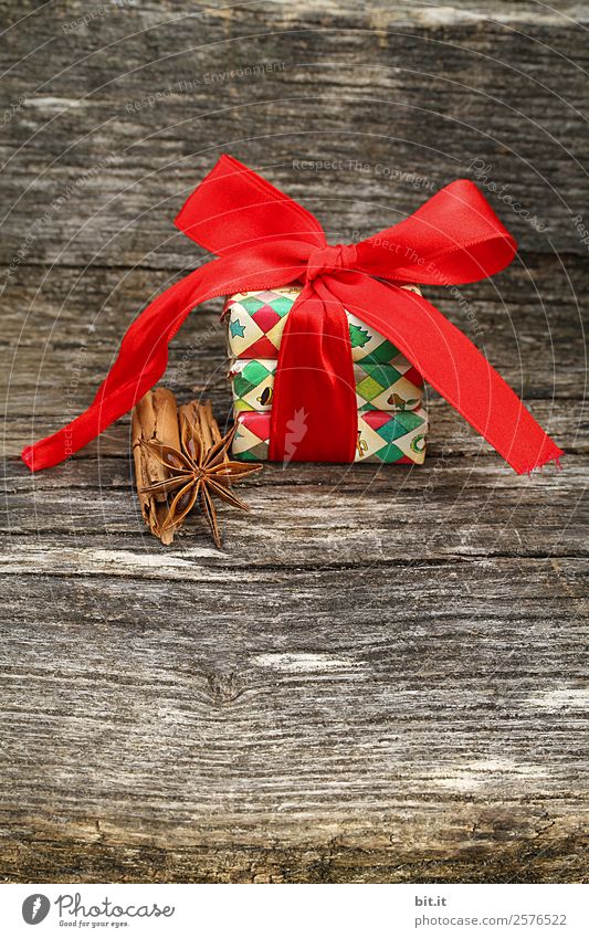 Überraschung l bunte Weihnachtspäckchen verpackt mit Weihnachtspapier mit roter Schleife, Zimt, Sternanis liegen auf rustikalem Holz. Weihnachtsgeschenk, liegt hübsch dekoriert mit großer Schleife aus rotem Band und weihnachtlichen Gewürzen auf Holztisch.