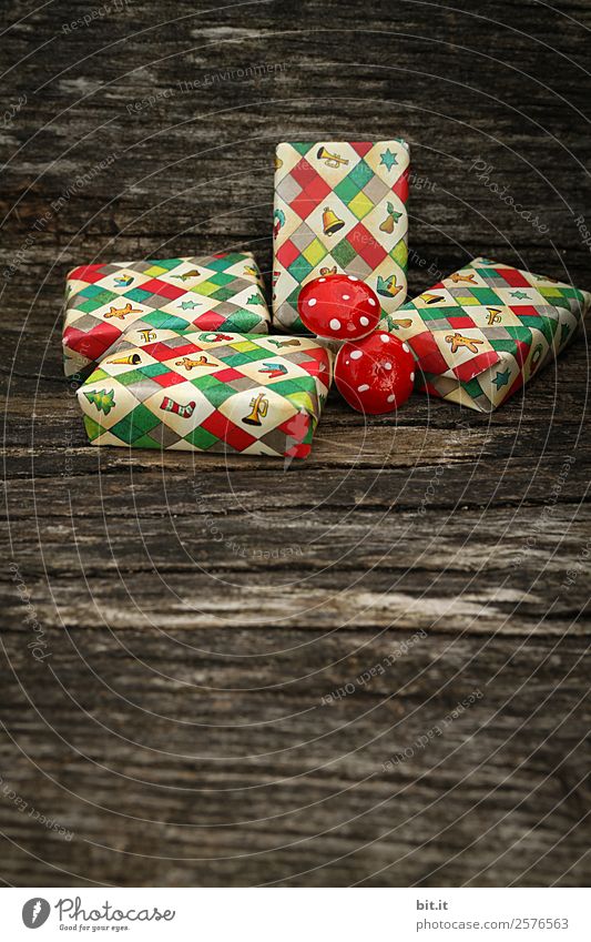 Überraschung l viele, bunte, umhüllte Weihnachtspäckchen & Pilze, liegen auf altem rustikalen Holztisch als Dekoration und Verzierung. Kleine Weihnachtsgeschenke in Geschenkpapier mit Weihnachtsmotiv verpackt, warten unterm Weihnachtsbaum aufs Auspacken.