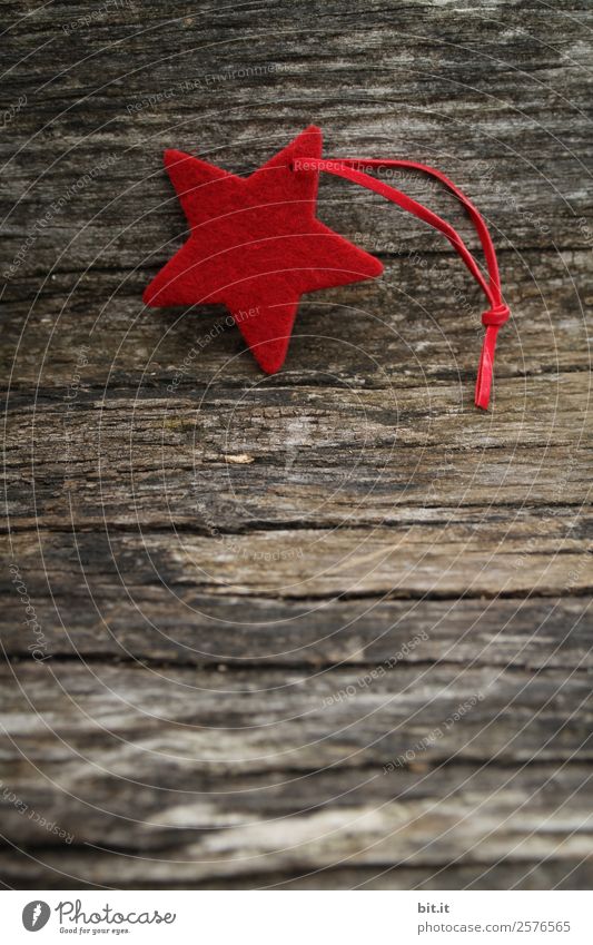 Frohe Weihnachten. Roter Stern aus Filz mit Band, liegt auf altem Holz. Roter Weihnachtsstern, als Dekoration auf rustikalem, braunen Holzbrett. Filz-Stoff-Stern als Schild, Blanko, Anhänger, Aufhänger auf braunem, rustikalem  Holztisch, Textfreiraum.